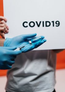 person wearing gloves holding vaccination needle with a sign written "COVID19" in the background.